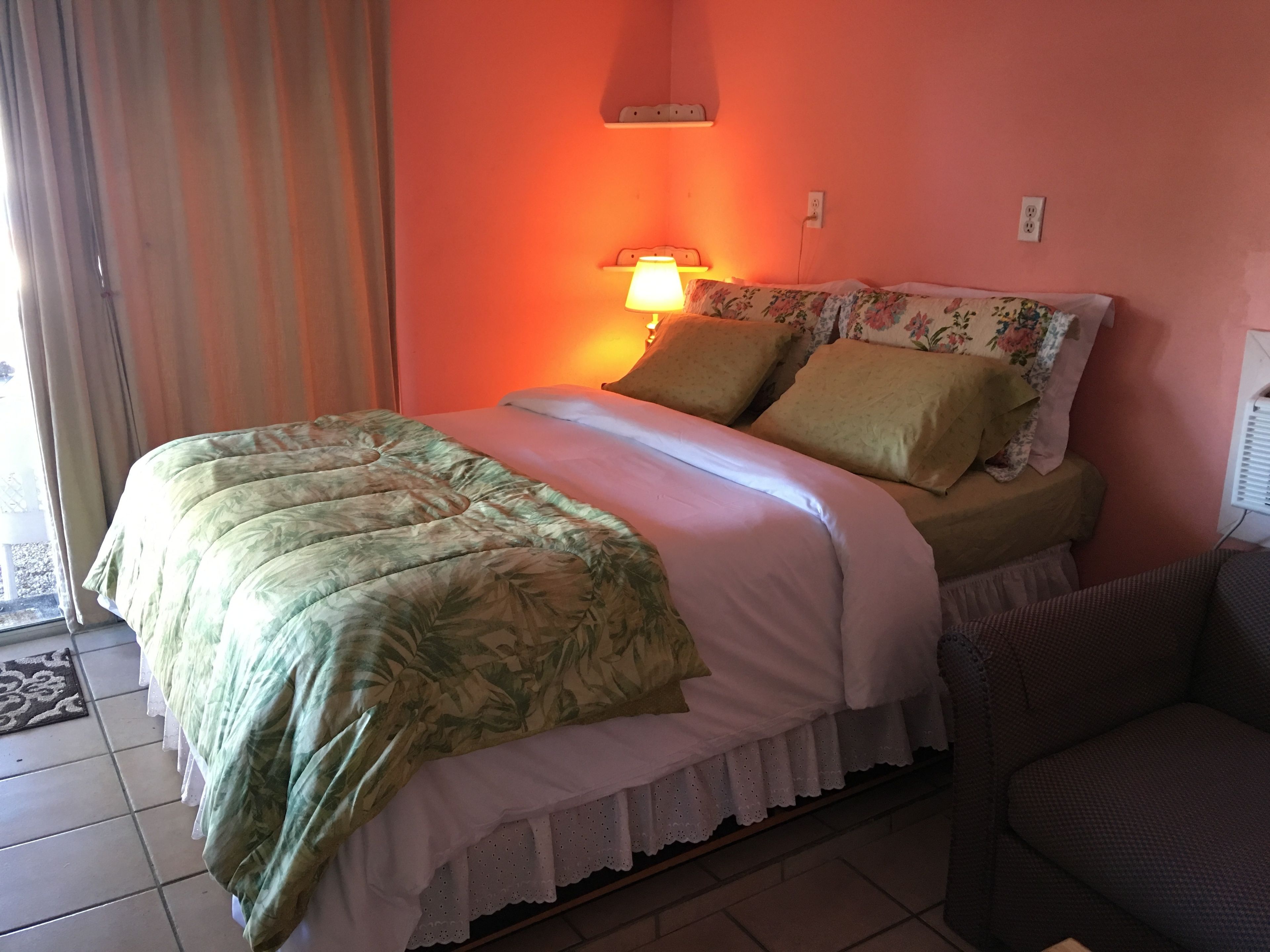 A bedroom with a bed, pillows, a nightstand, a lamp, and a window with curtains.
