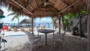 Un patio junto a la playa con techo de paja, una mesa y sillas.