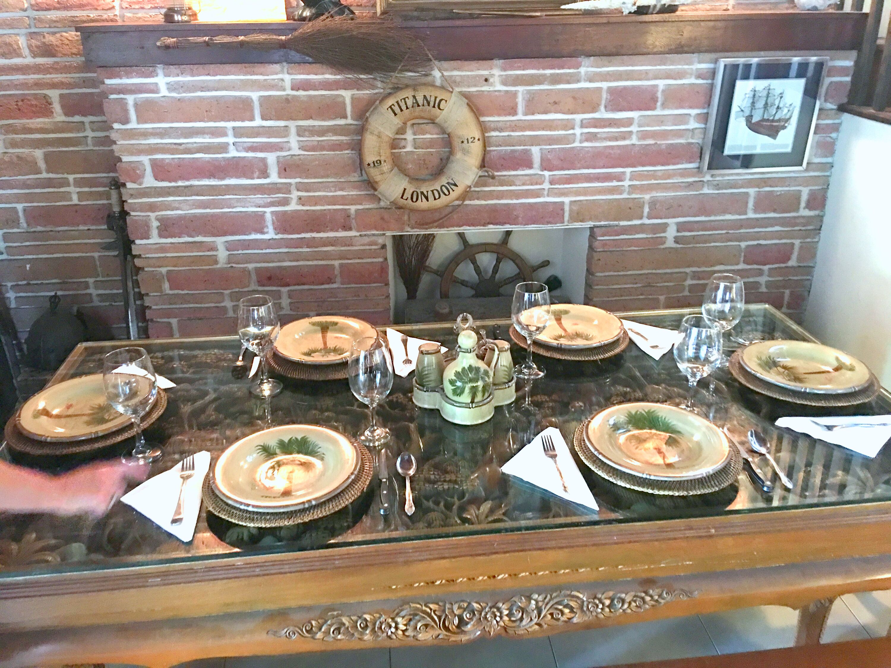 Une table à manger dressée avec des assiettes, des verres et des couverts, avec un mur de briques et un objet décoratif en forme de bouée de sauvetage en arrière-plan.