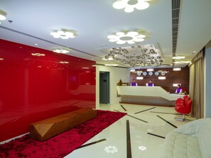 Et moderne receptionområde med en rød accentvæg, en træbænk og en reception med to medarbejdere.