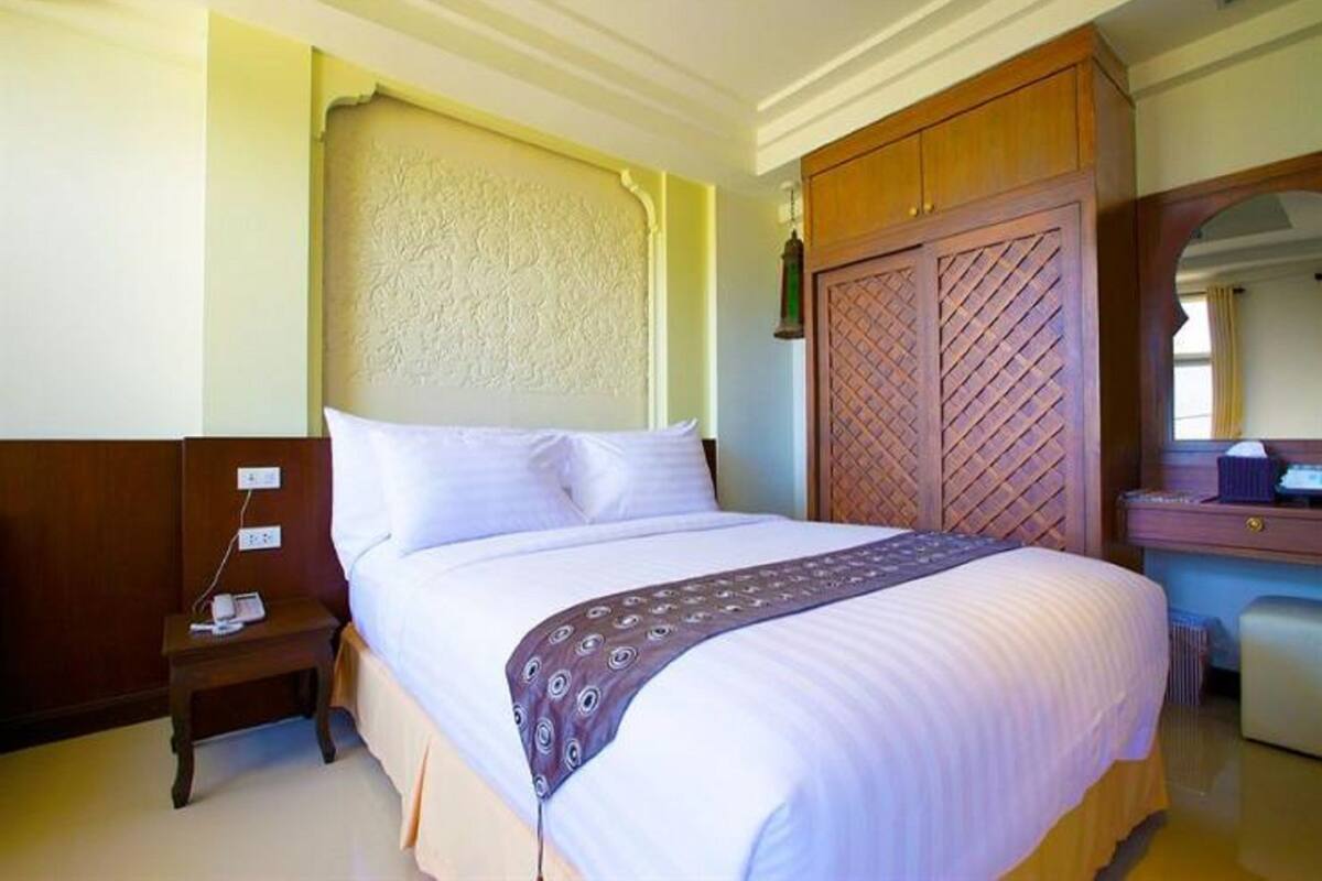 Un lit bien fait, recouvert d’un couvre-lit à motifs, une table de chevet en bois avec un téléphone, et une armoire au motif ajouré.