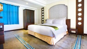 A hotel room with a large bed, a wooden wardrobe, a blue curtain, and a patterned rug.
