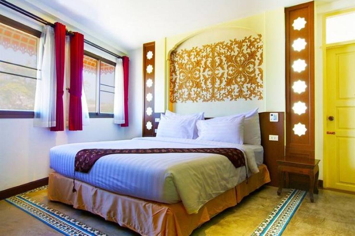 Une chambre d’hôtel avec un grand lit, une tête de lit à motifs, une petite table de chevet et une fenêtre avec des rideaux.