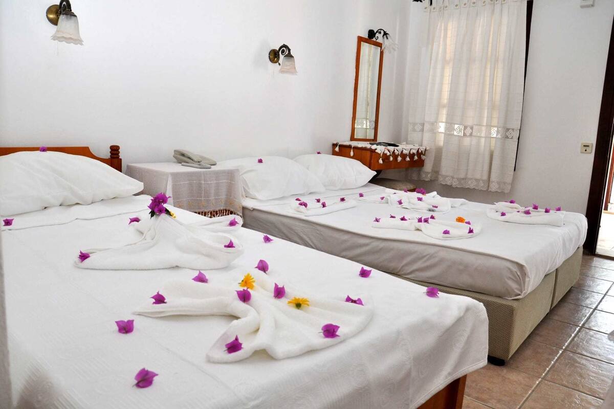 A hotel room with two beds, each adorned with white linens and towels, and scattered with purple and yellow flowers.