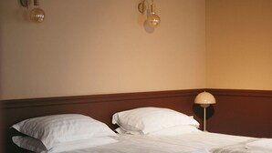 Une chambre d’hôtel avec deux lits, une tête de lit en bois et des lampes fixées au mur.