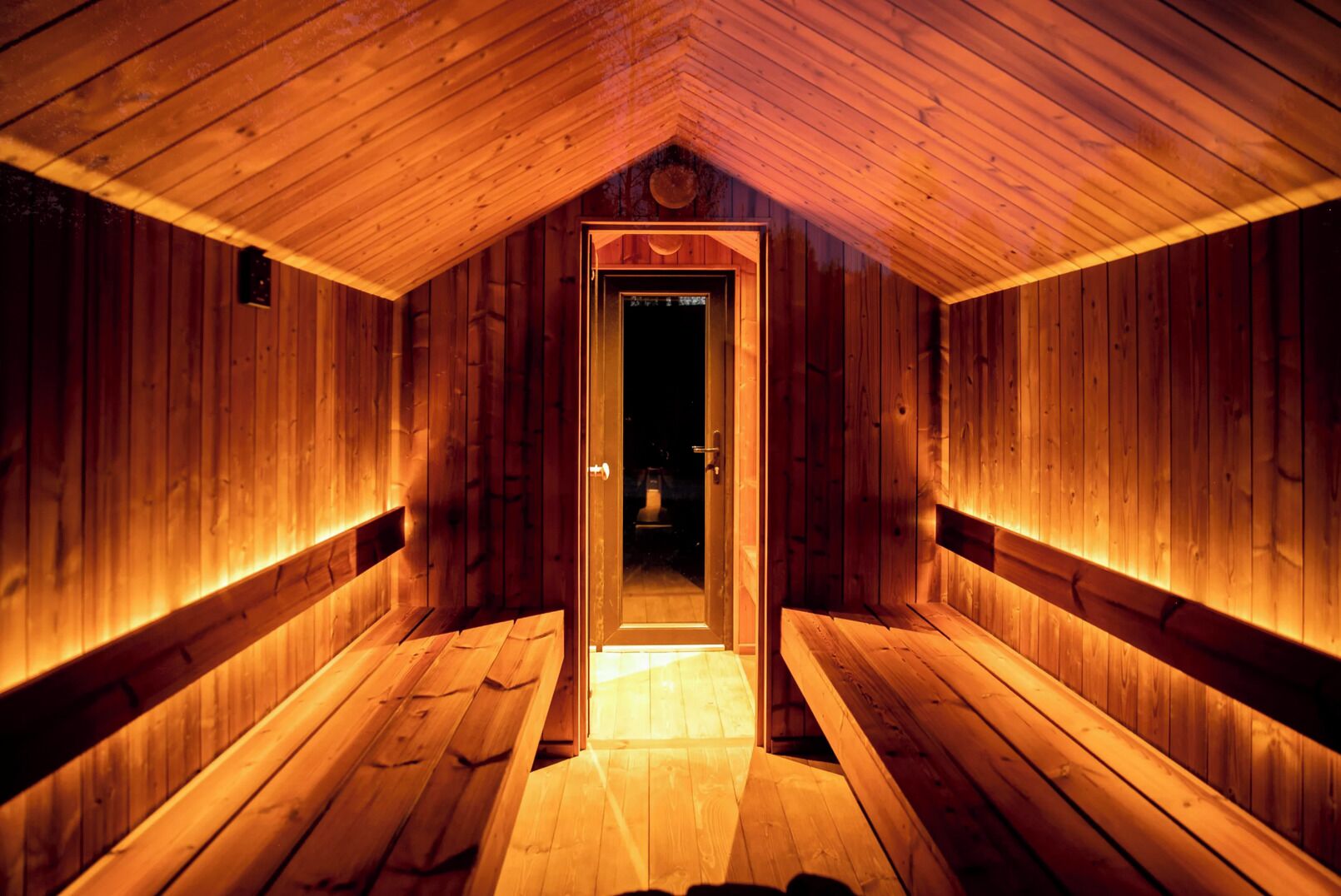 Eine Holzsauna mit einer Bank und einer Tür zu einem dunklen Raum.