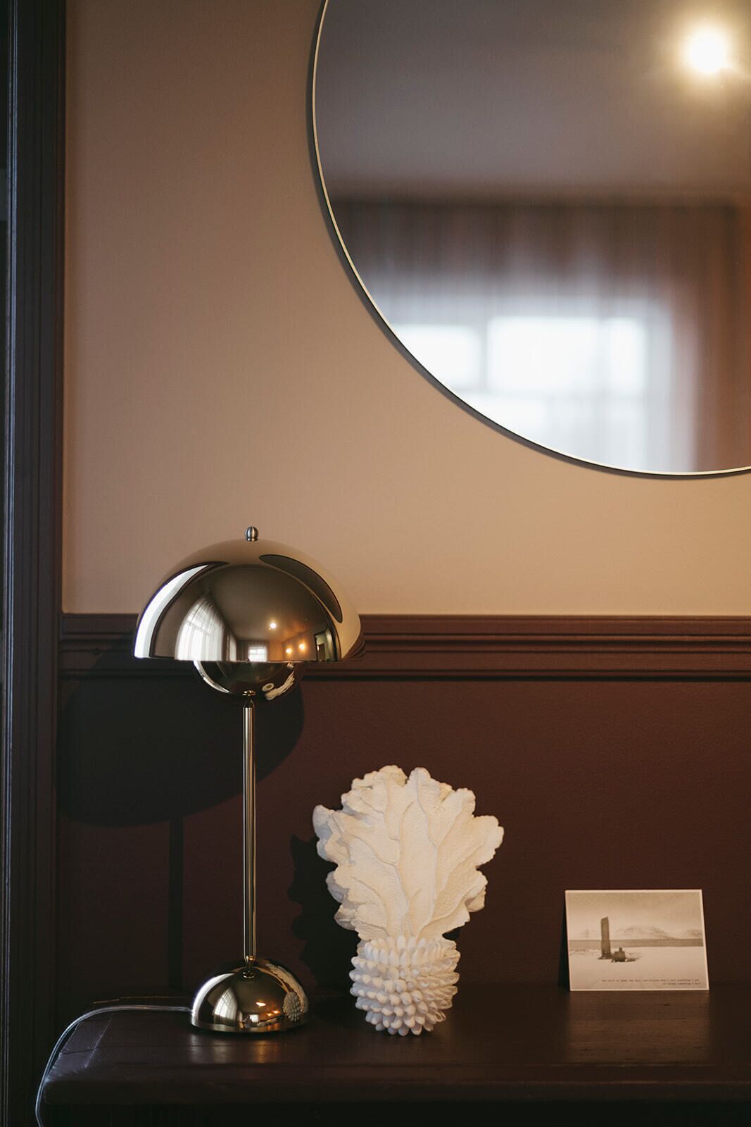A lamp, a decorative object, and a postcard on a wooden surface.
