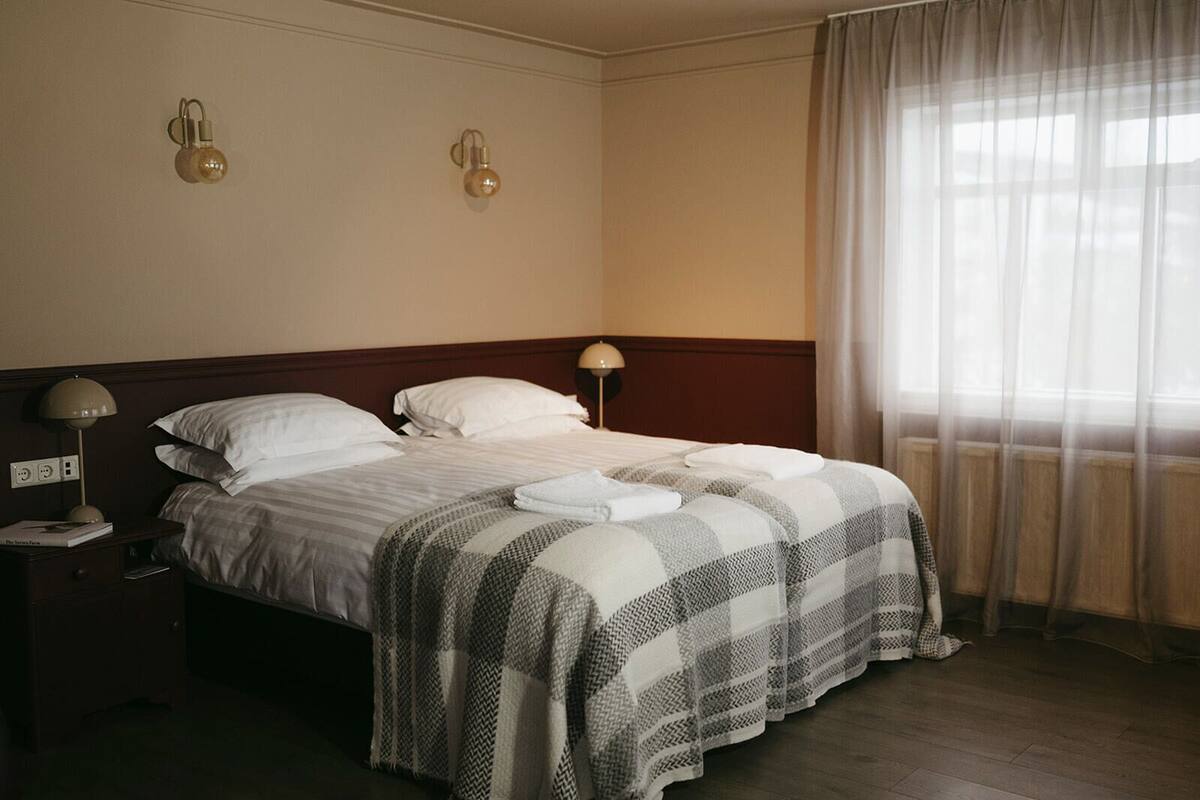 A neatly made bed with a checkered blanket, a bedside lamp, and a nightstand with a book.