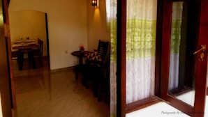 A room with a dining table and chairs, a small table with a vase, and a window with curtains. - Sana Guest (Weligama)