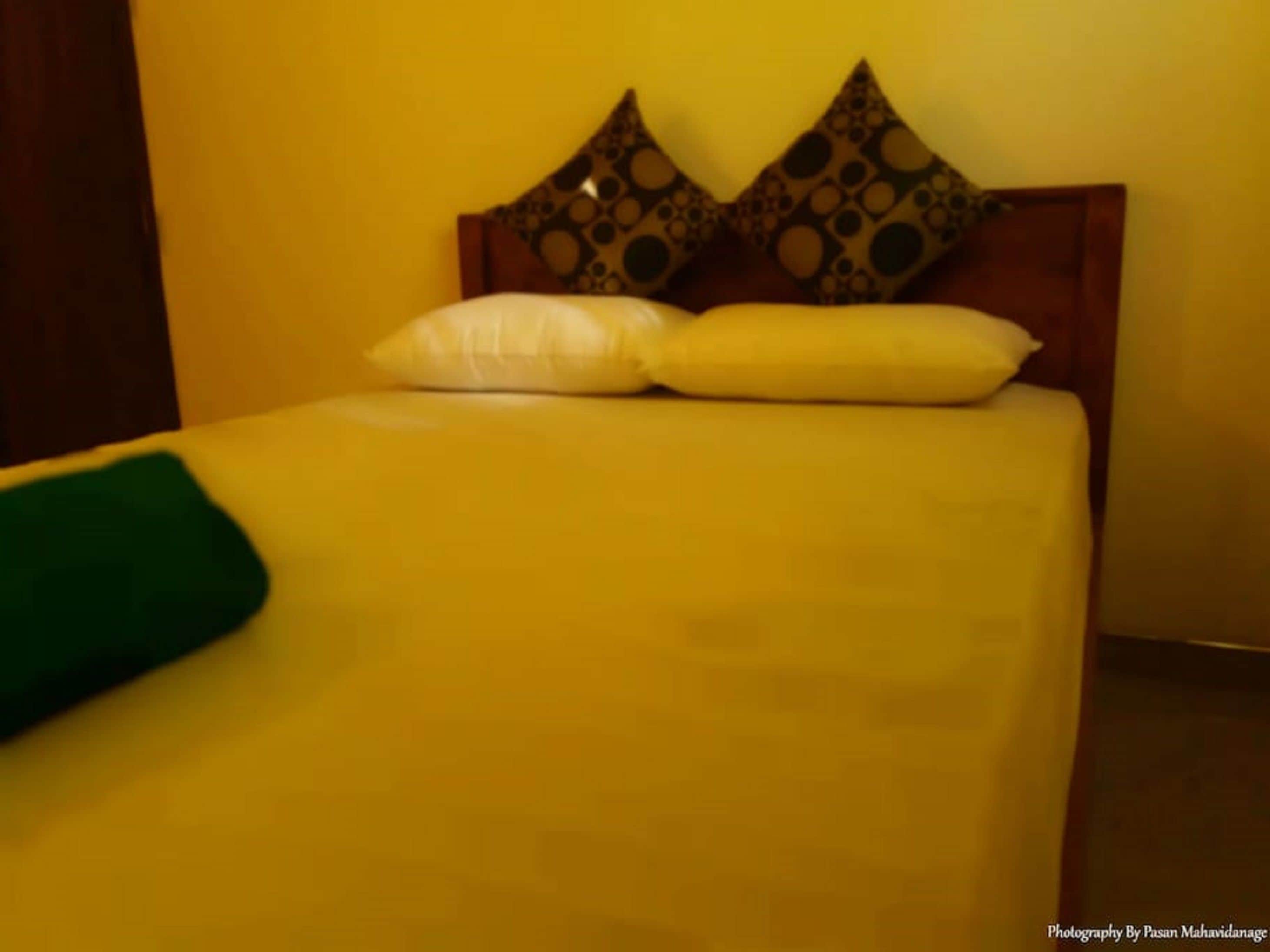 Ein Bett mit Holz-Kopfstück, zwei Kissen und einer grünen Tagesdecke.
