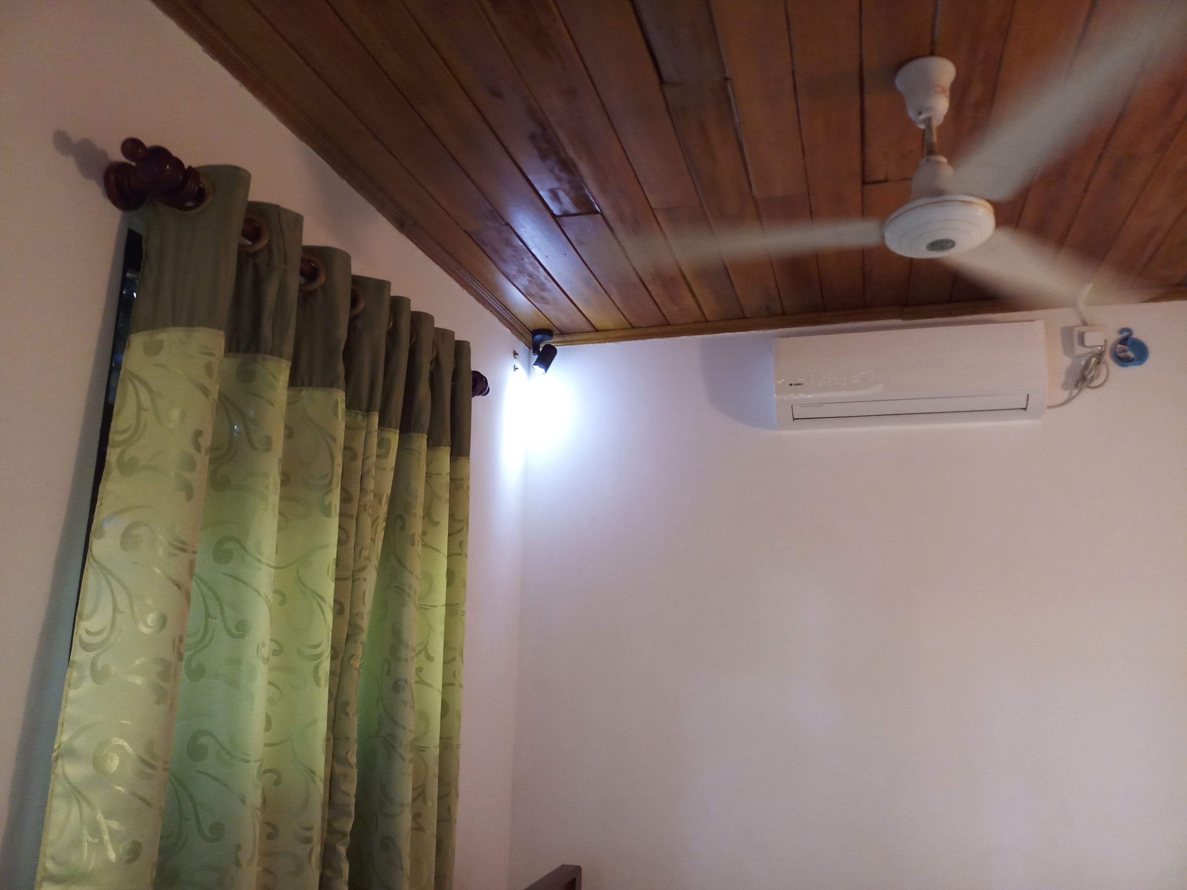 Una habitación con ventilador de techo, aire acondicionado y cortinas estampadas.
