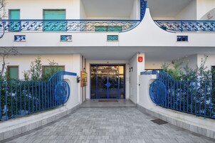 L'ingresso di un edificio con un cancello in metallo blu, un vialetto piastrellato e una facciata bianca.