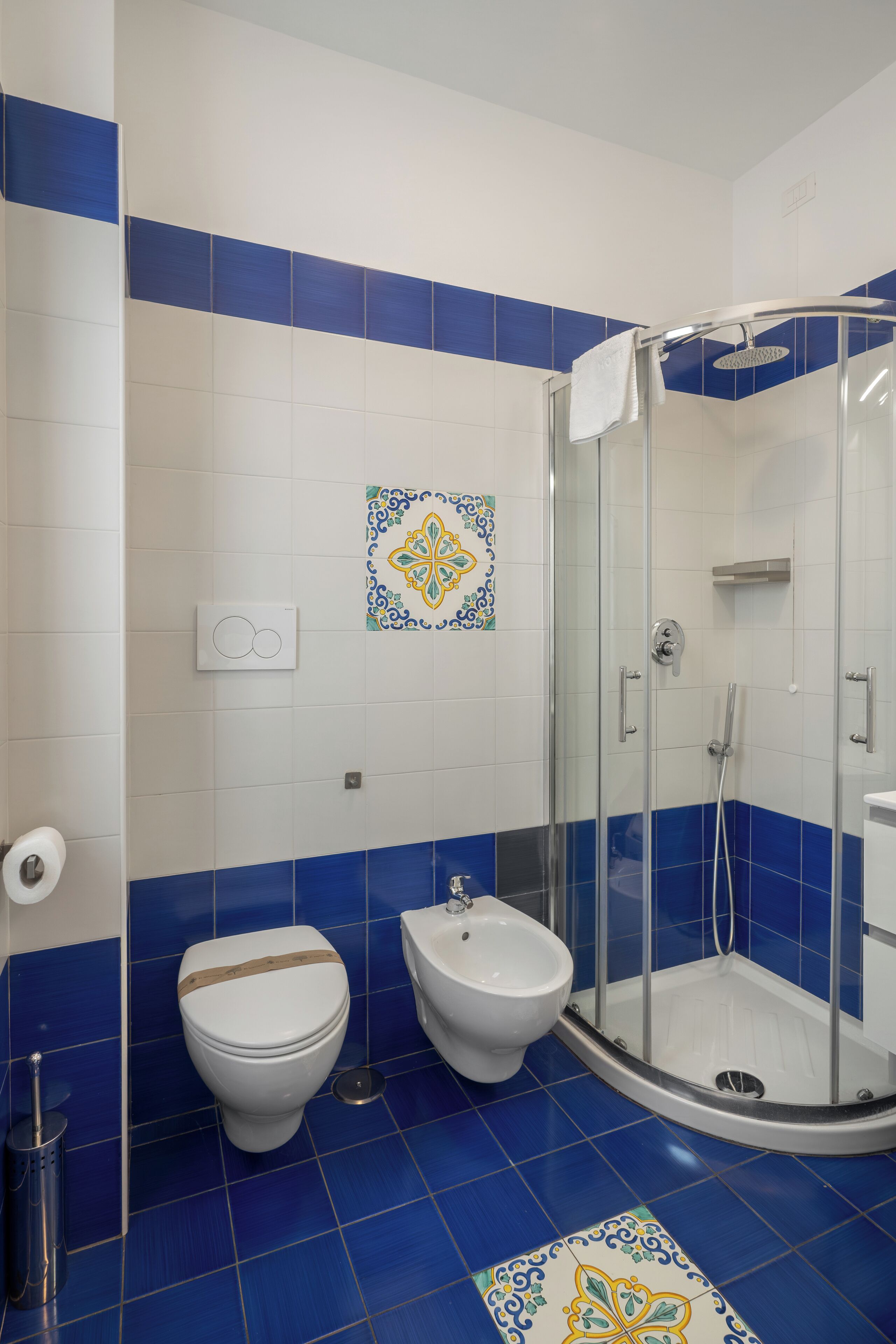 Une salle de bain équipée d’une douche, de toilettes, d’un bidet et d’un mur recouvert de carreaux décoratifs.
