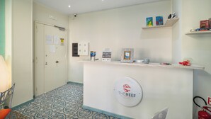 Zona de recepción con mostrador que muestra un logotipo, extintor y manguera contra incendios. Se ven estanterías con libros y objetos decorativos, además de un suelo con diseño.