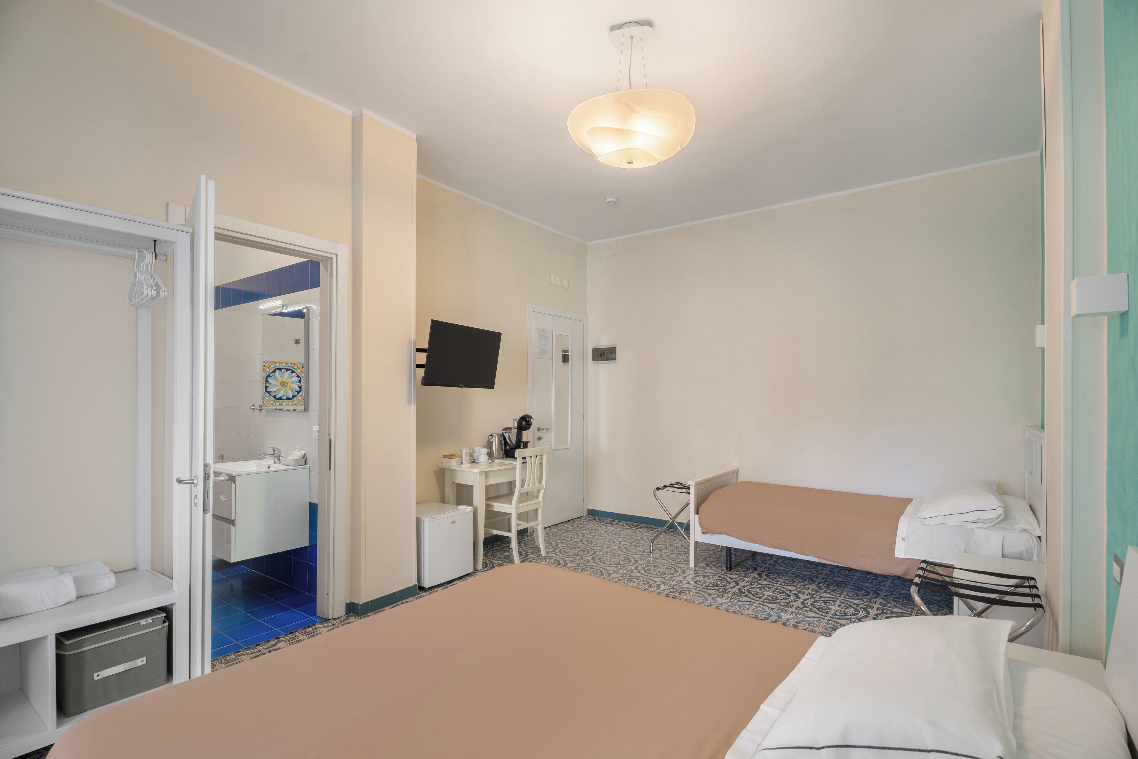Een hotelkamer met een bed, een bureau, een stoel, een klein keukentje en een badkamer.