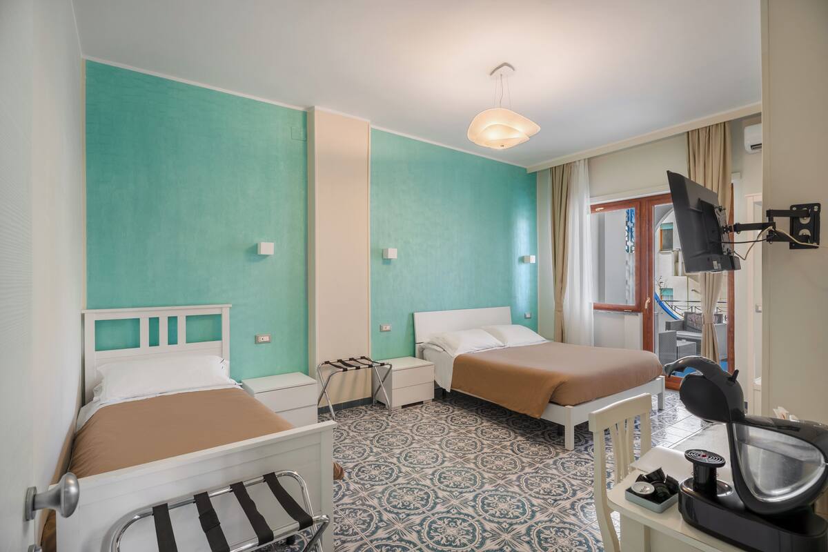 A hotel room with two beds, a desk with a chair, a TV mounted on the wall, and a patterned floor.