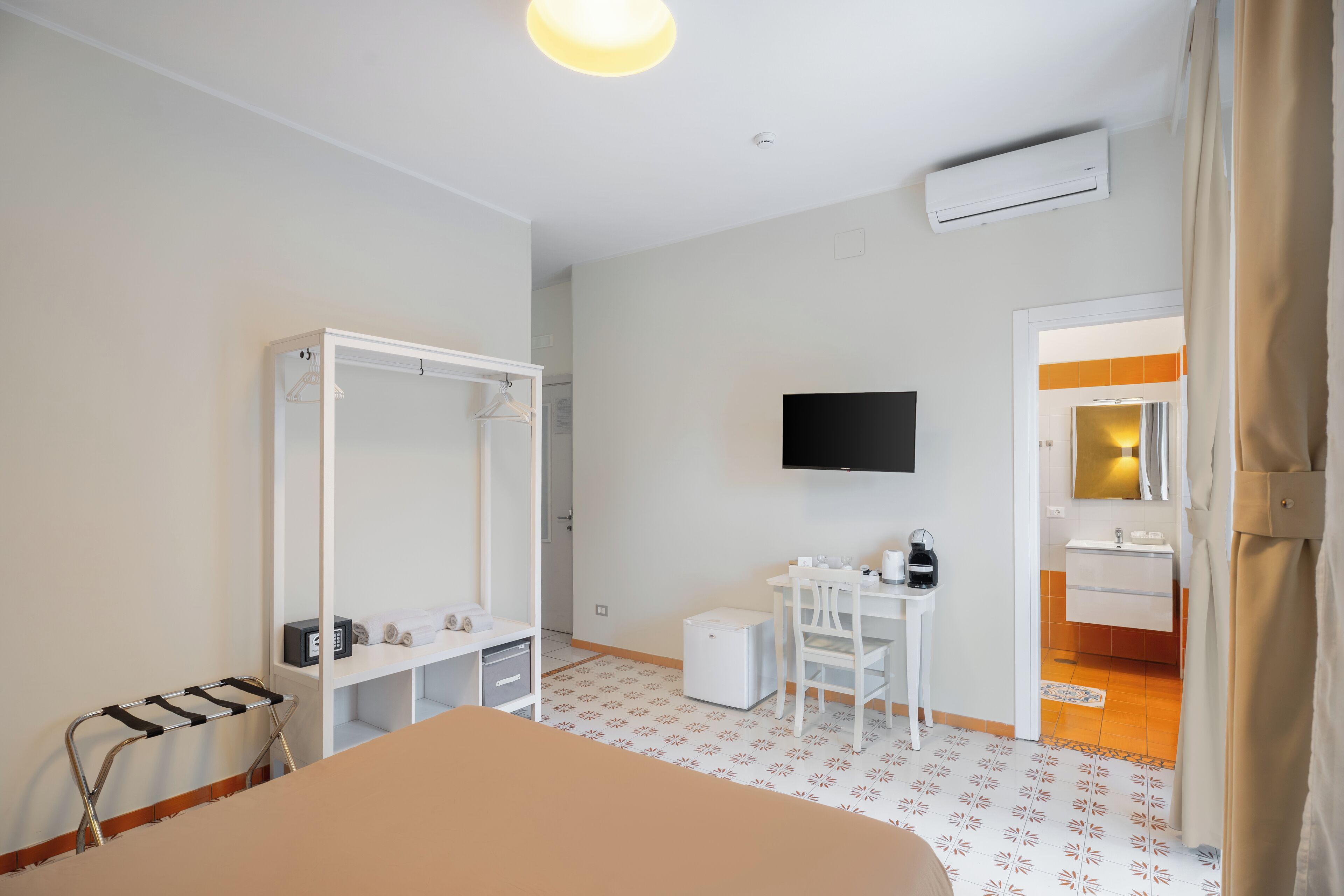 Ein Hotelzimmer mit einem Bett, einem Schreibtisch, einem Sessel, einem Fernseher, einem Kleiderschrank und einem durchgegangene Tür sichtbaren Badezimmer.