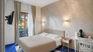Habitación de hotel con cama, escritorio, silla, cafetera y vista al balcón exterior.