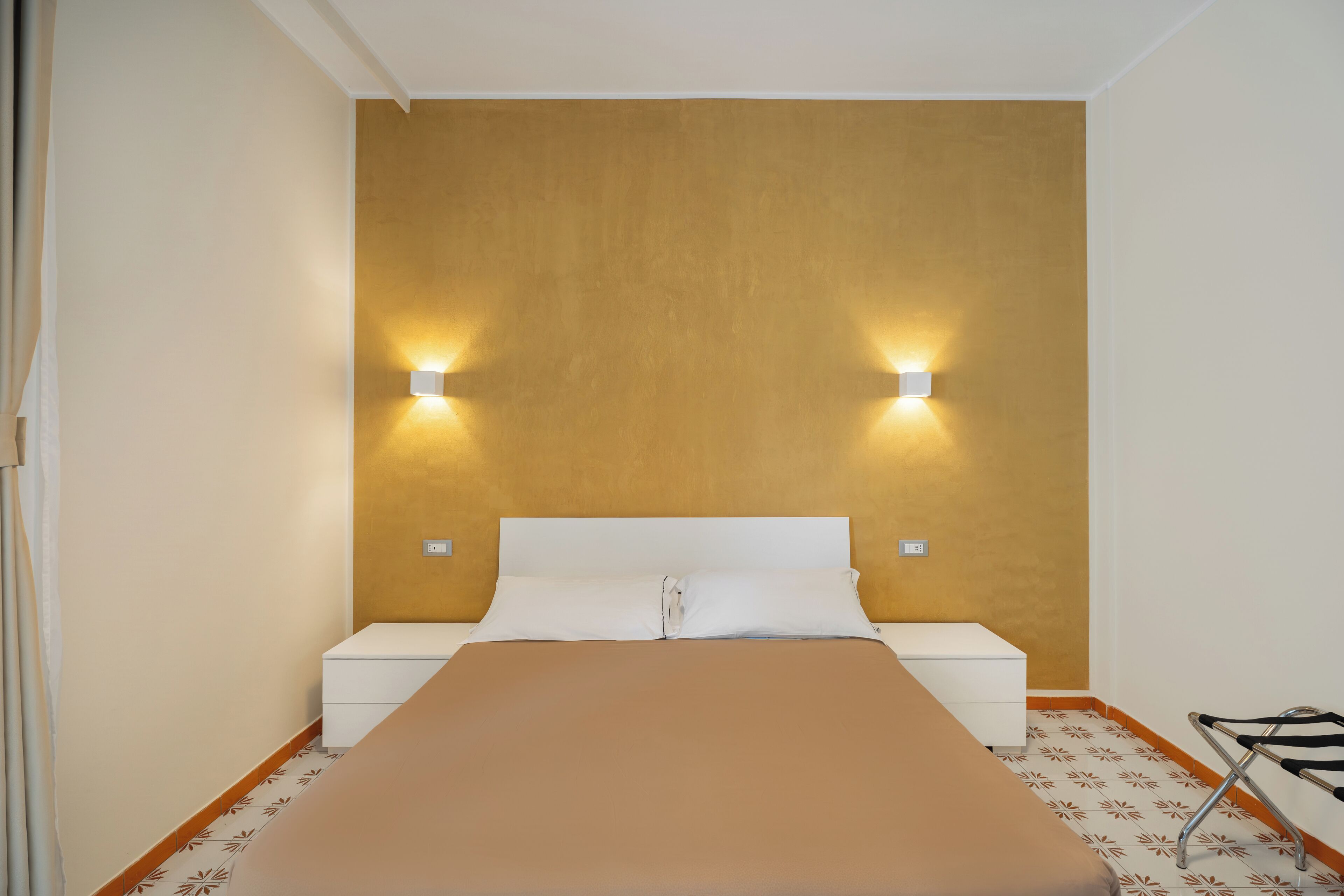 Un dormitorio con una cama, dos mesitas de noche y luces fijadas a la pared.