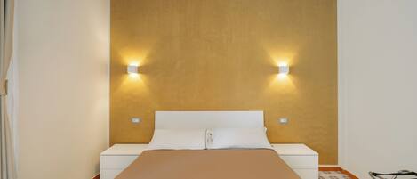 Un dormitorio con una cama, dos mesitas de noche y luces fijadas a la pared.