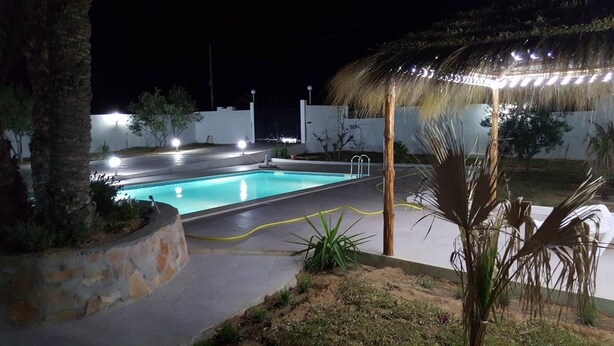 A swimming pool at night with surrounding vegetation and a covered area. - Villa La Fidèle (Aghir)