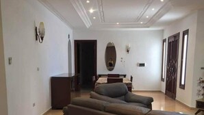 A spacious living area with a large sofa, a staircase with marble steps, and a chandelier. - Villa La Fidèle (Aghir)
