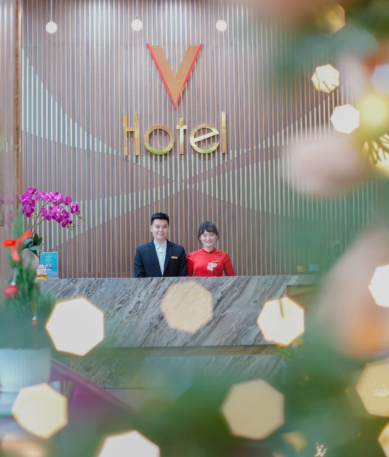 A reception desk with a 'Hotel' sign above, a marble counter, and a floral arrangement to the left.
