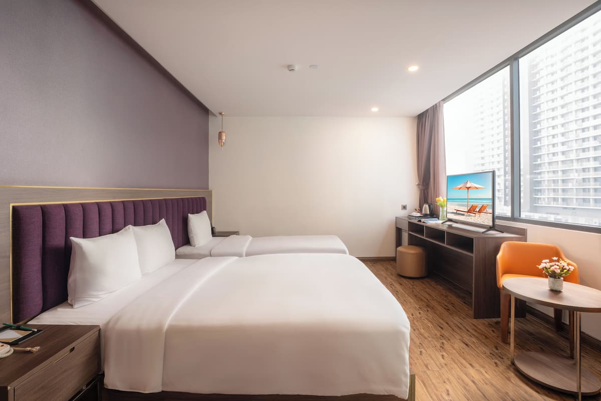 A hotel room with two beds, a desk, a chair, a TV, and a large window with a city view.