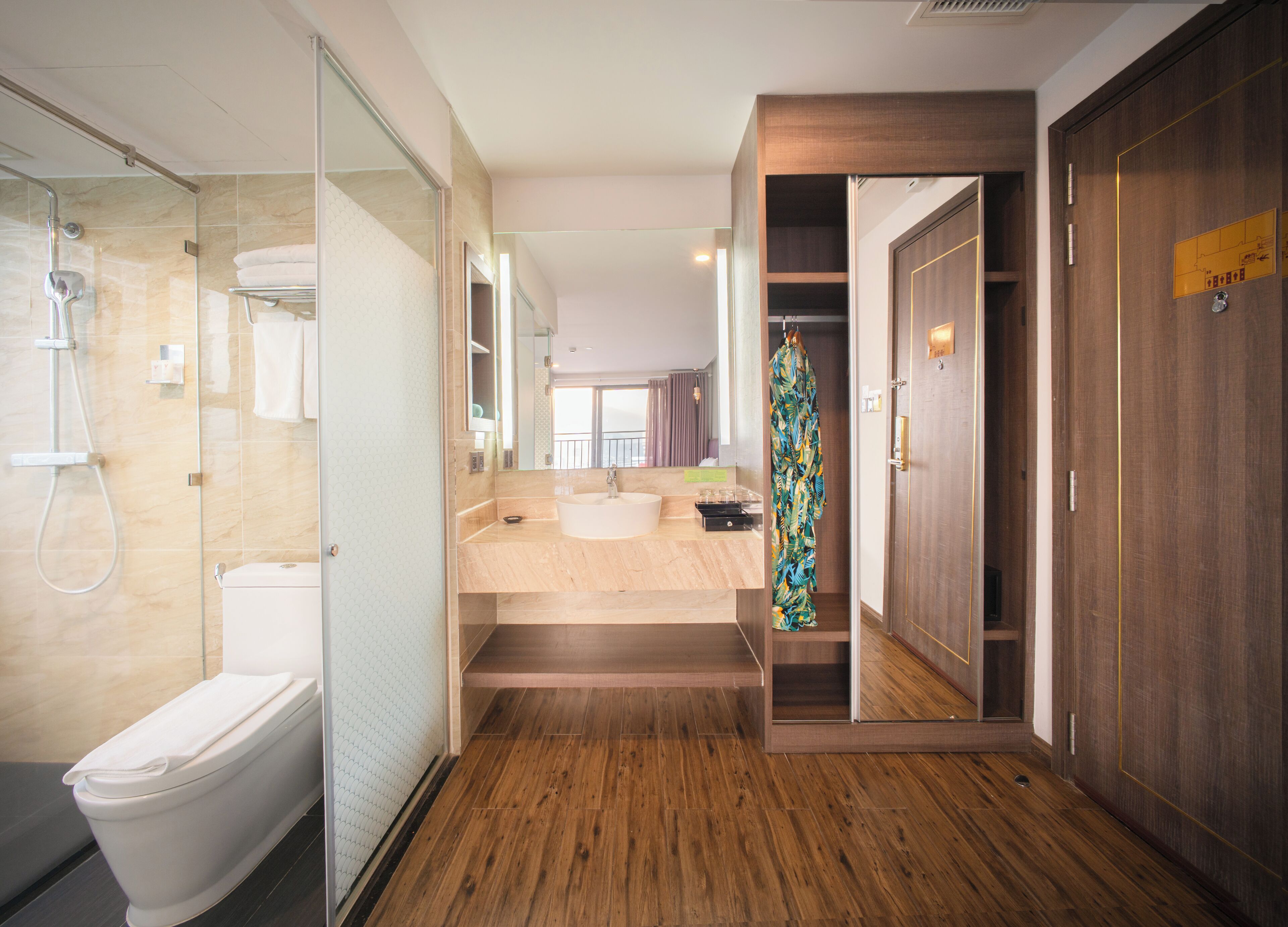 A modern bathroom with a glass shower enclosure, a white toilet, a wooden vanity with a sink, and a walk-in closet with a wooden door.