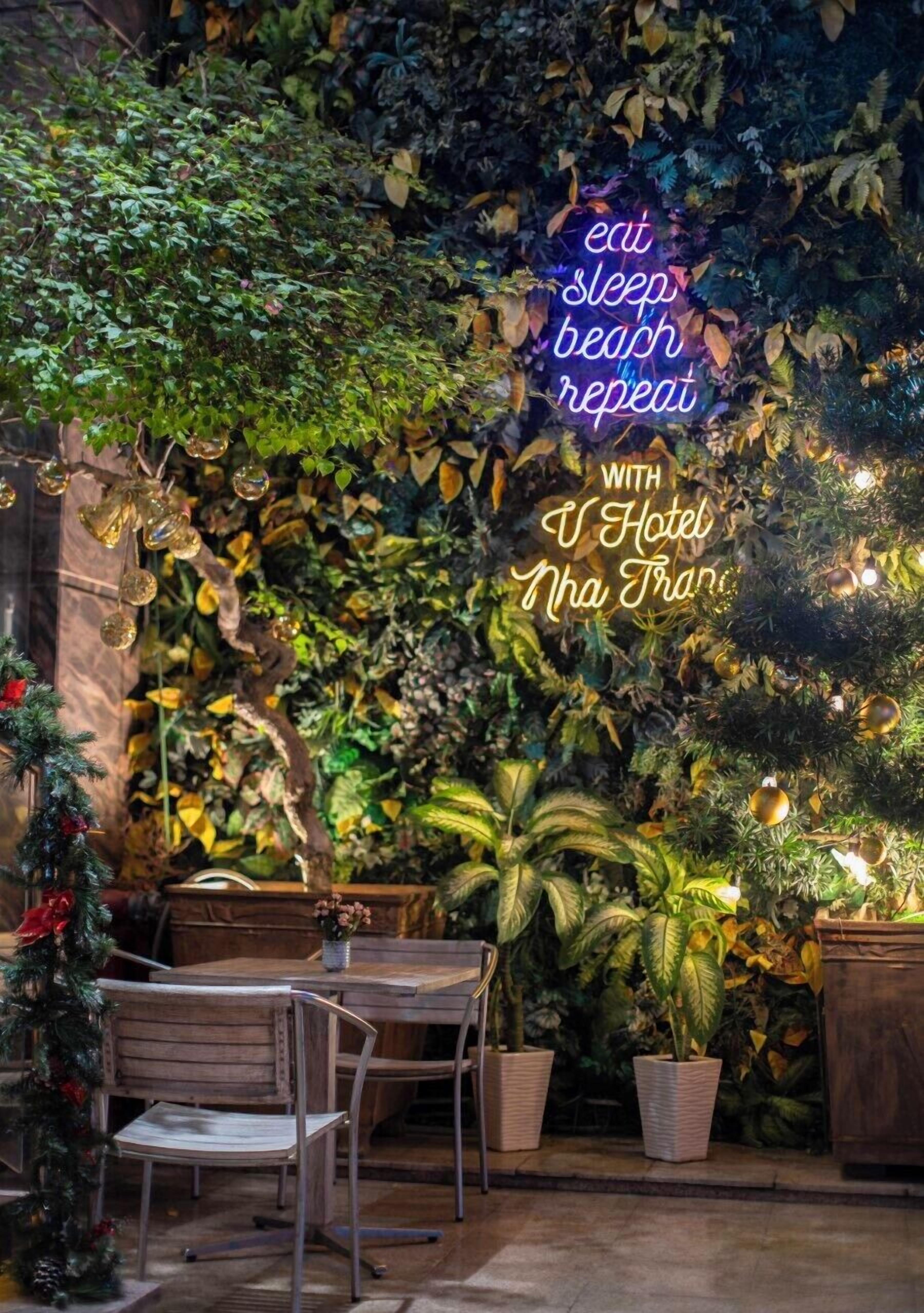 A cozy indoor seating area with a neon sign reading "eat sleep beach repeat" and "with Hotel Nha Trang".