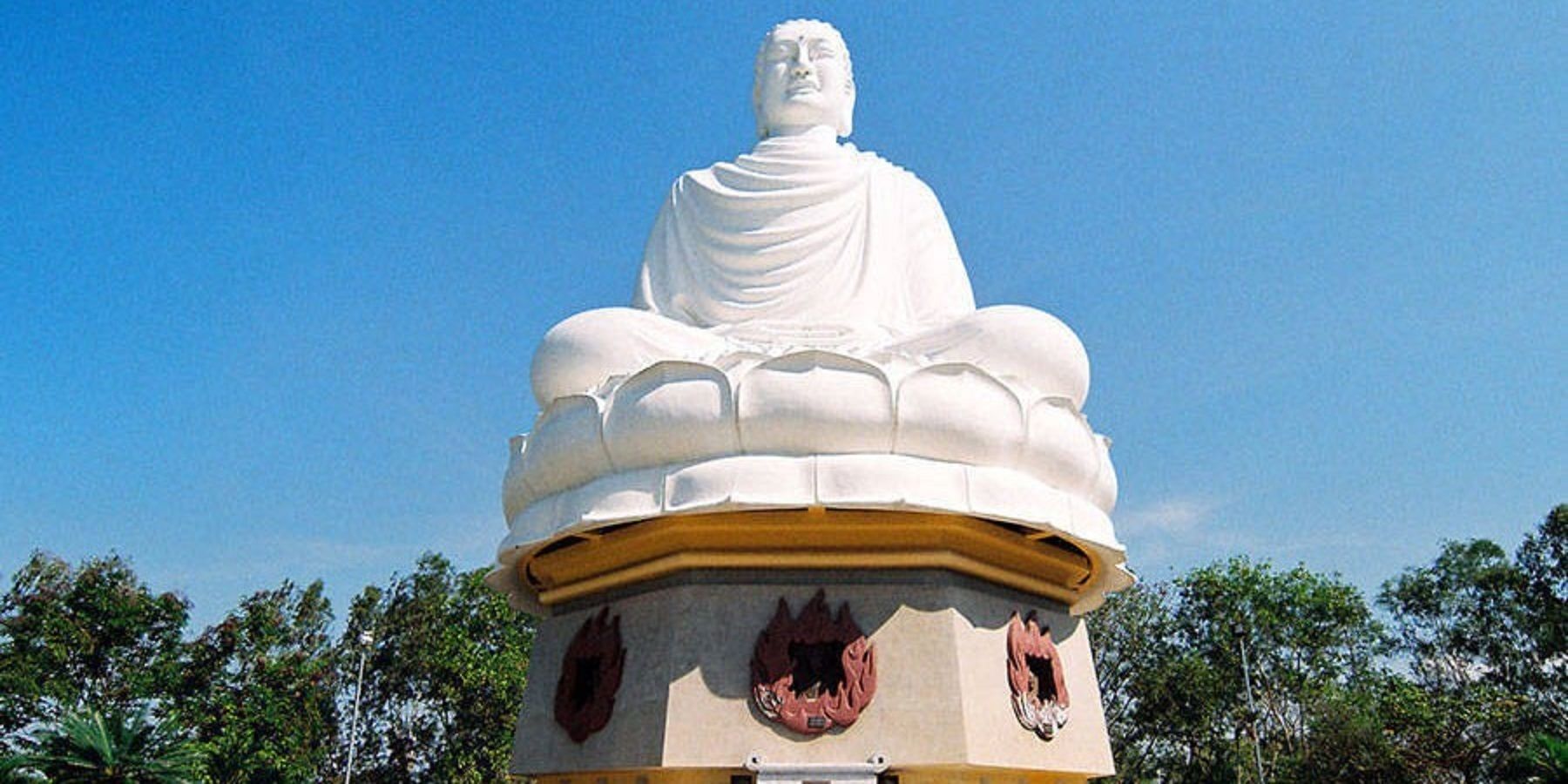 A large white statue of a seated figure on a pedestal with a clear sky in the background.