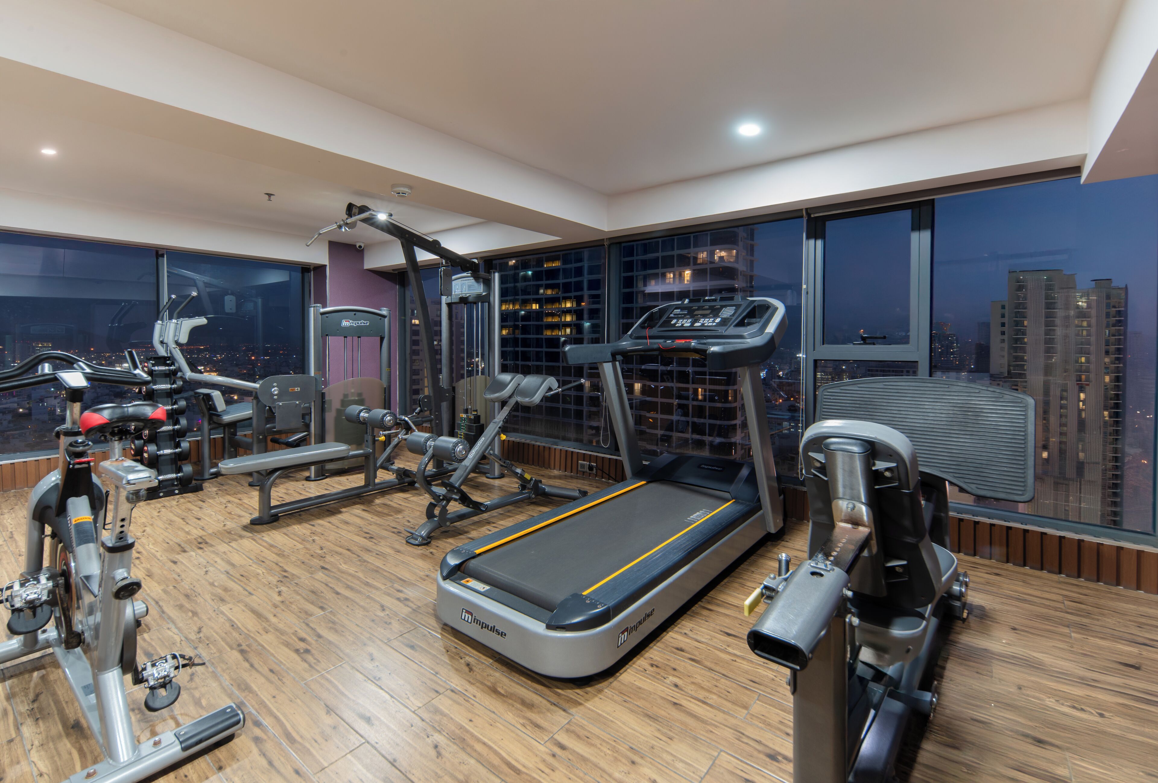 A modern gym with various exercise equipment, large windows, and a city view.
