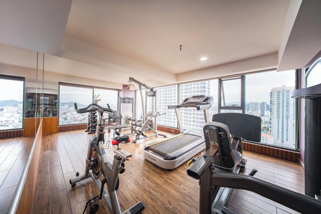 Une salle de sport moderne dotée de divers équipements d’exercice, de grandes fenêtres et offrant une vue sur la ville.
