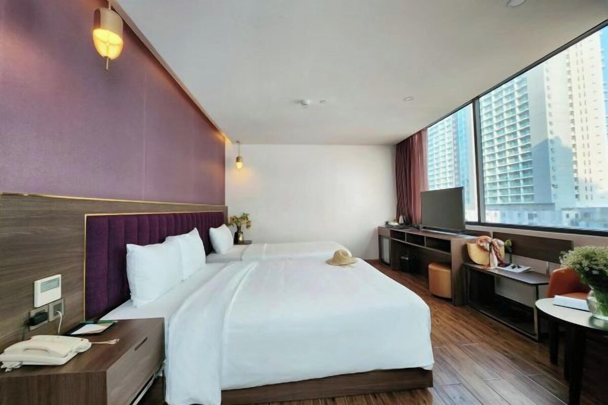 A hotel room with a large bed, a desk, a chair, a TV, and a window with a city view.
