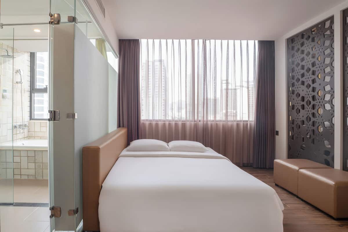 A modern hotel room with a large bed, a glass shower enclosure, a seating area, and a decorative wall panel.