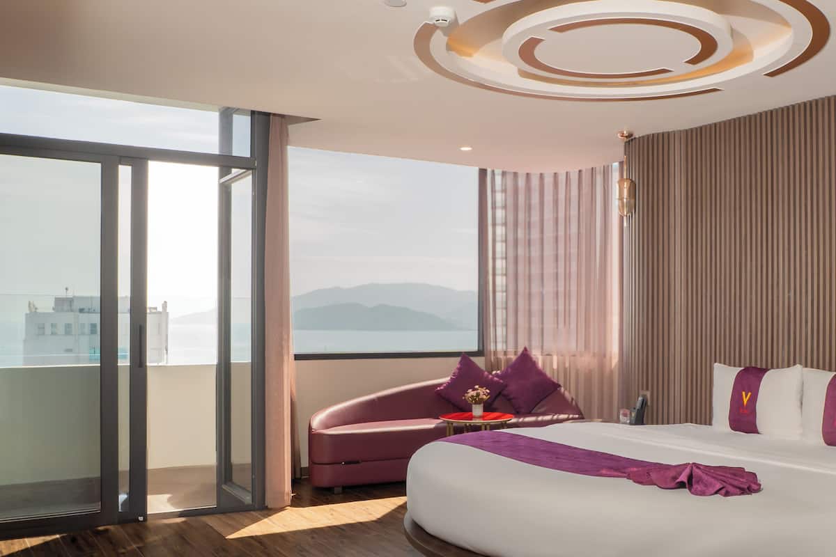 A modern hotel room with a large bed, a seating area, and a view of the city.