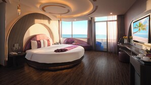 Quarto de hotel moderno com uma cama grande, vista para o mar e televisão na parede.