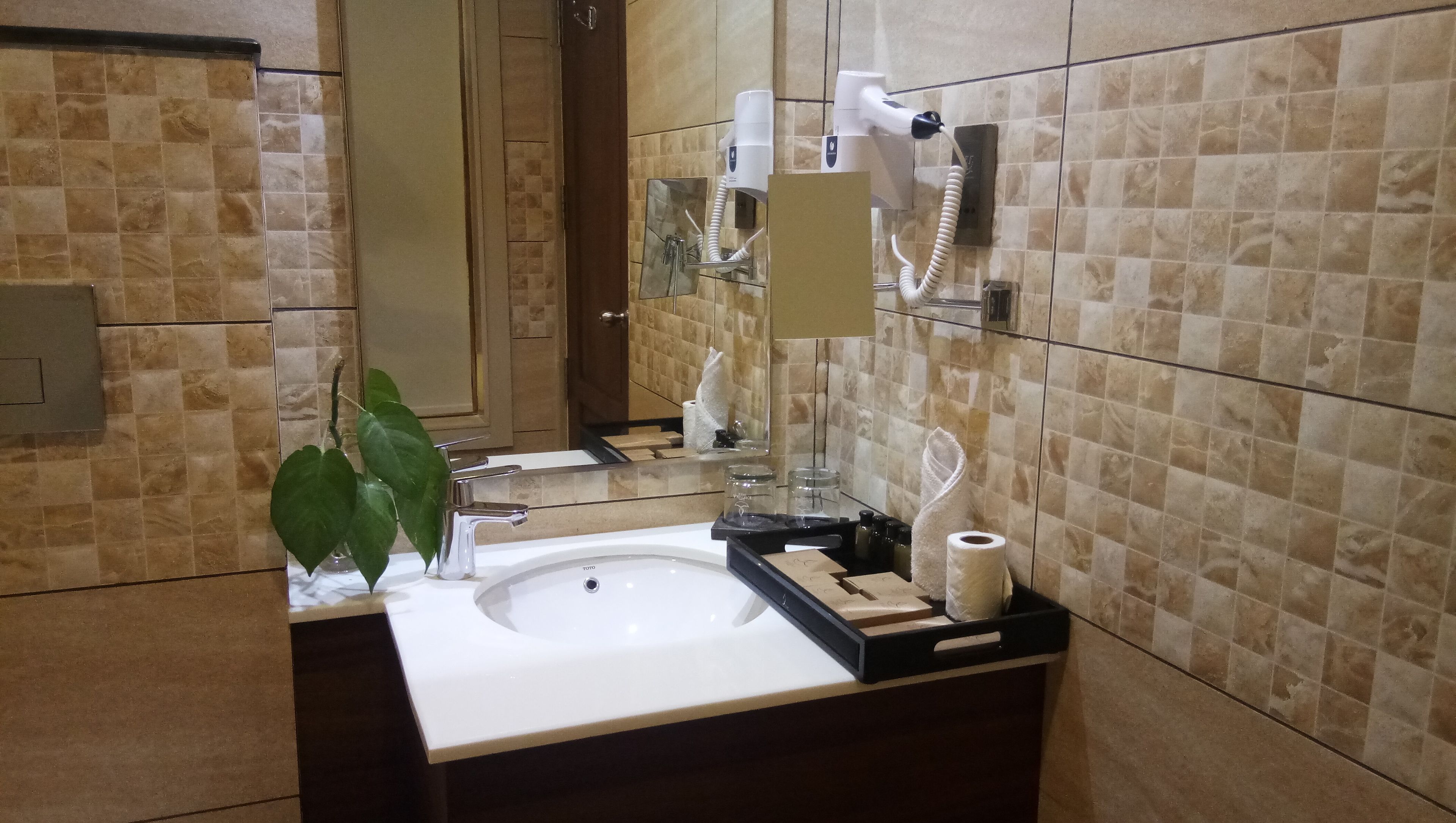 Uma casa de banho com uma pia branca, um espelho, um porta-toalhas e um secador de cabelo.