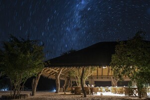 A thatched-roof structure with outdoor seating and a view of the starry night sky.