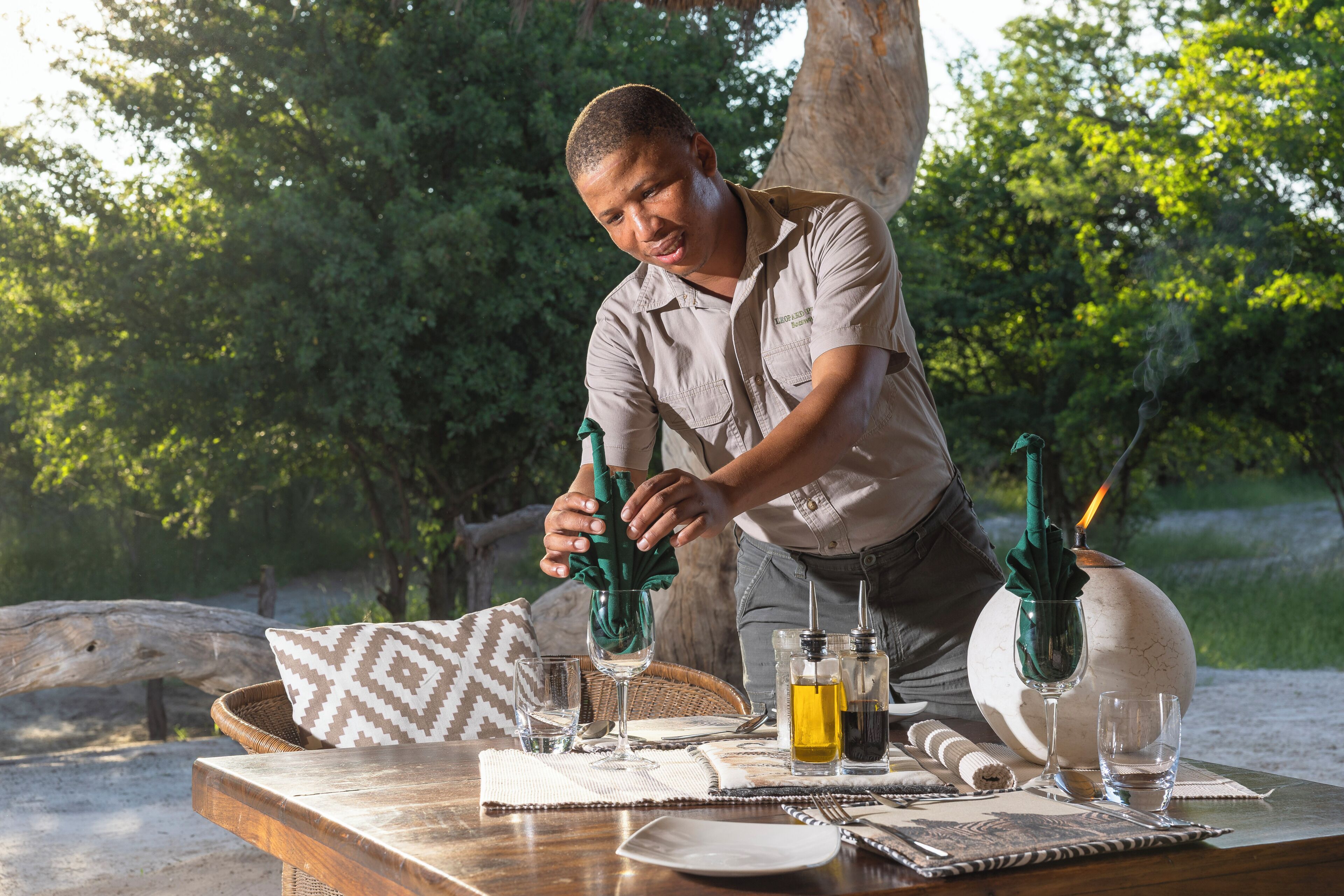A dining table set outdoors with a bottle of olive oil, a candle, and a glass.