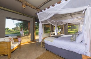 A bedroom with a canopy bed, a wooden bench, and a large window overlooking greenery.