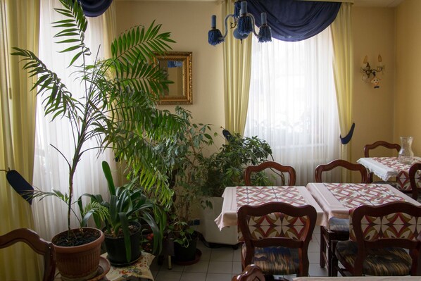 A dining area with multiple tables and chairs, surrounded by potted plants.