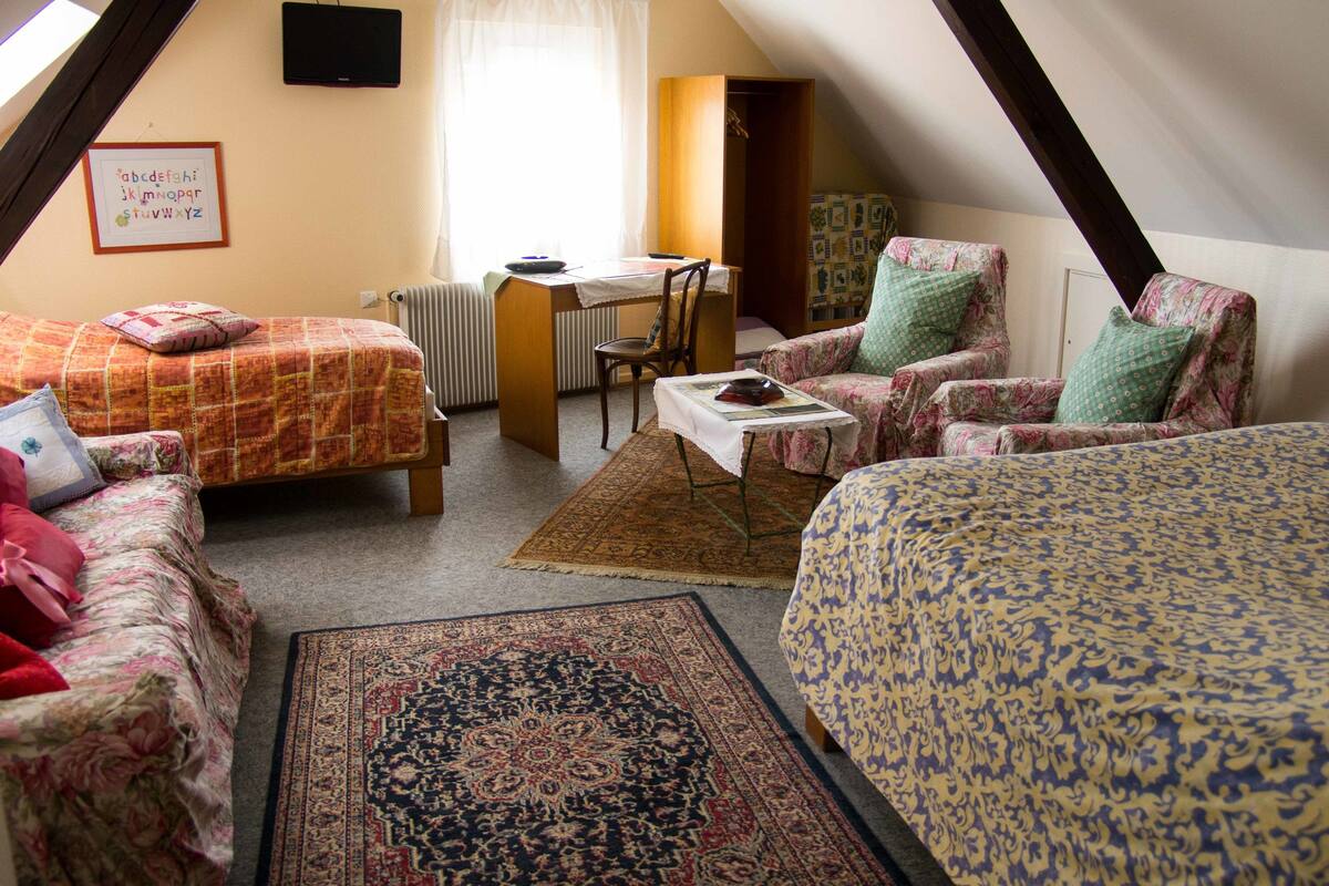 A cozy attic bedroom with two beds, a desk, and a chair.