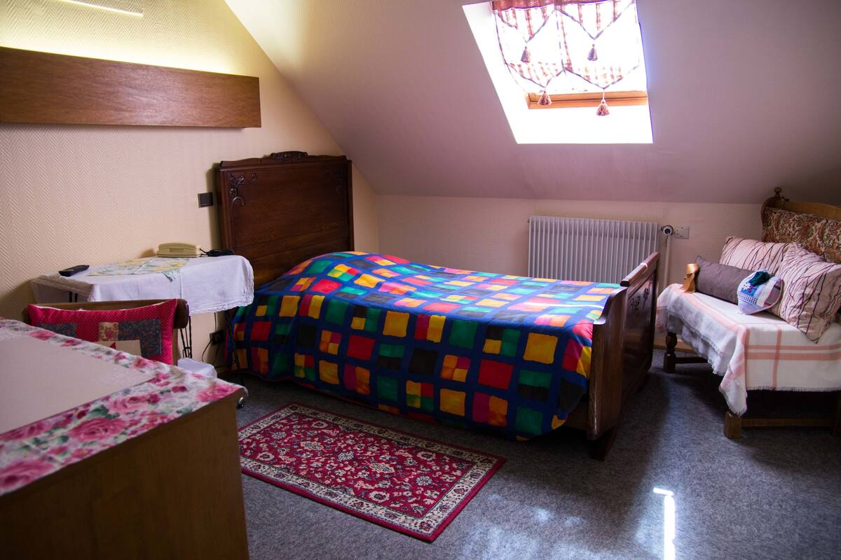 A bedroom with a bed, a nightstand, a dresser, a window with a view, and a radiator.