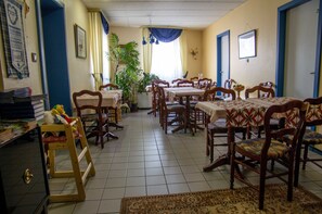 A dining area with multiple wooden tables and chairs, a potted plant, and a tiled floor. - Hôtel de Bâle (Bantzenheim)