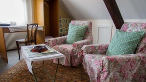 A cozy room with a wooden chair, a floral armchair, and a small table with a book and a teapot. - Hôtel de Bâle (Bantzenheim)