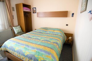 A bedroom with a bed, a wardrobe, a bedside table with a lamp, and a radiator. - Hôtel de Bâle (Bantzenheim)