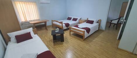 A hotel room with two single beds, a wooden desk, a small table, and a chair.