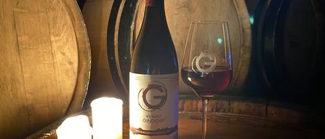 Una botella de vino y una copa sobre una superficie de madera, con velas y barriles al fondo.