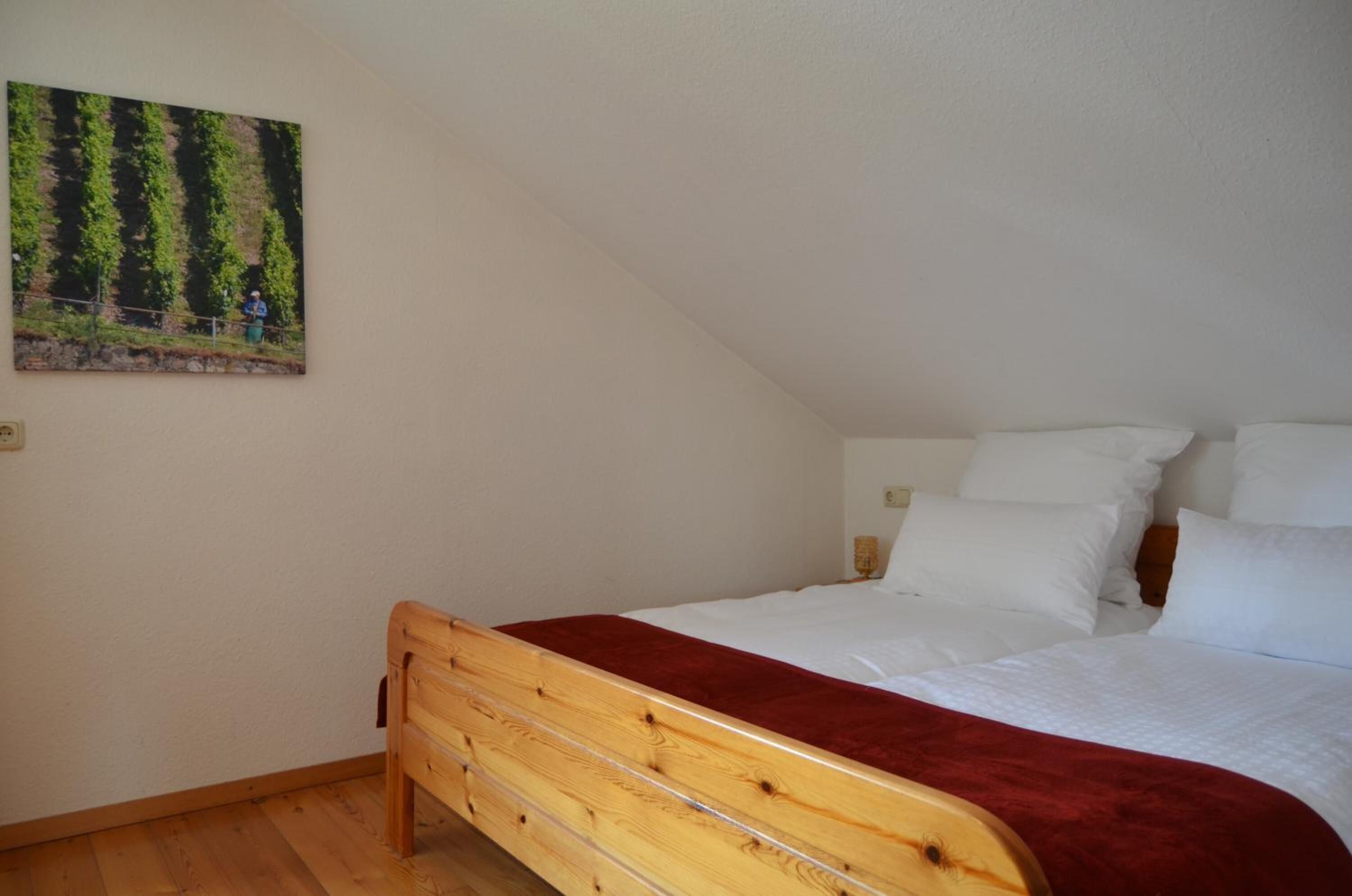 A bedroom with a wooden bed, white bedding, and a painting of a forest scene on the wall.